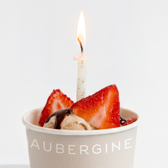 A small Nice Cream topped with fresh strawberries and a lit birthday candle, served in an Aubergine cup